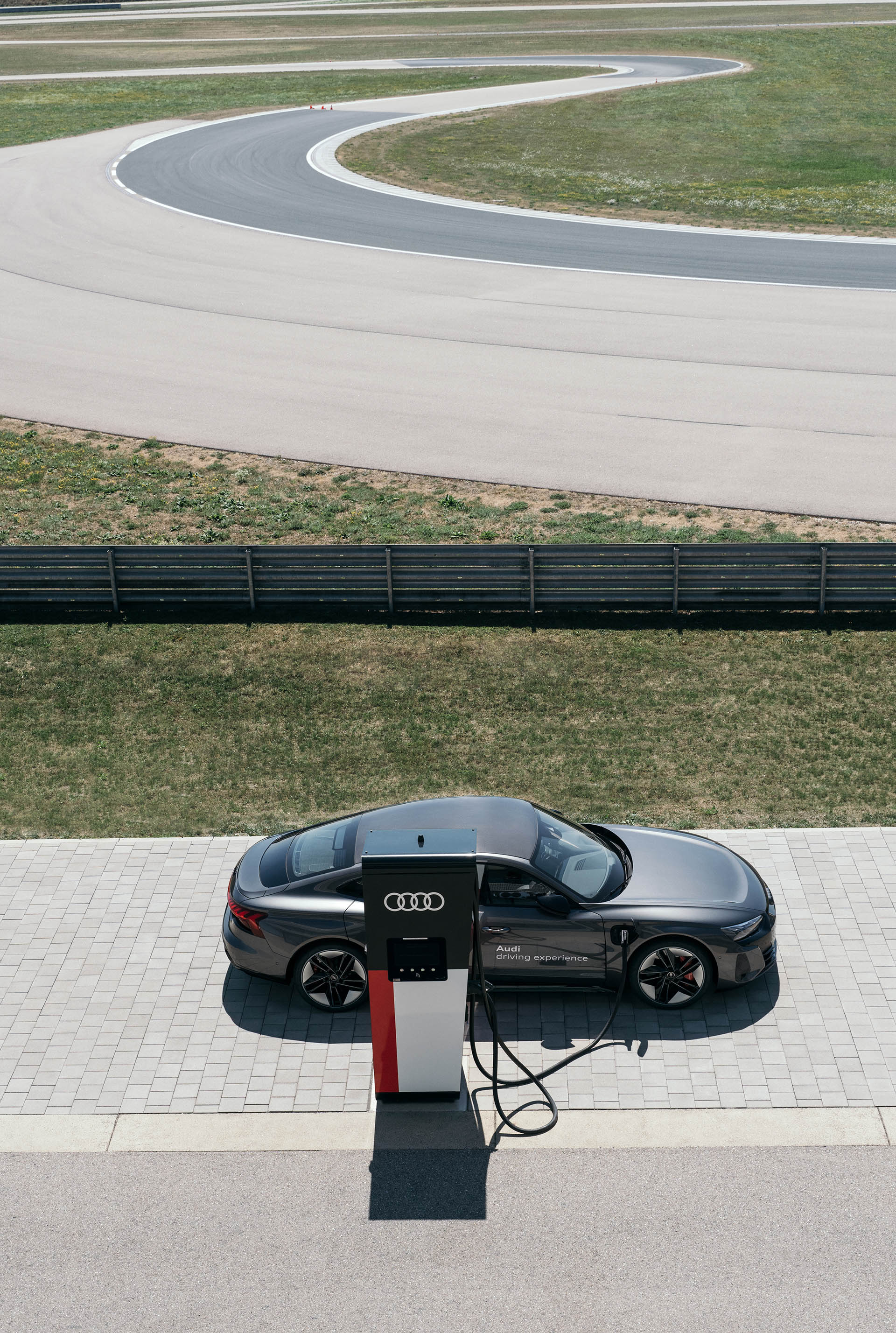 Audi RS e-tron GT ön planda şarj oluyor, arka planda yarış pisti görülebiliyor.