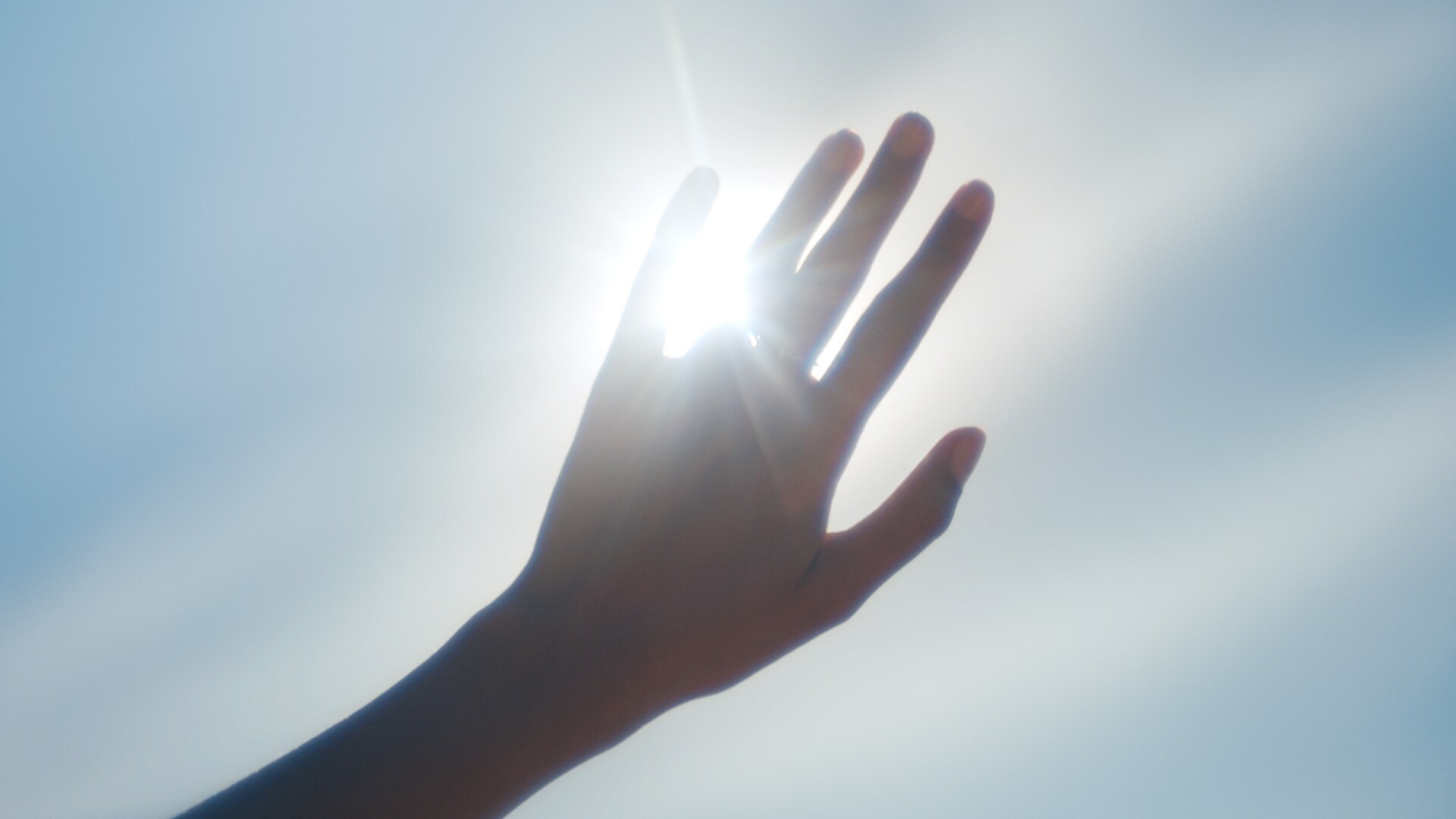 Güneş ışığı bir elin parmaklarının arasından süzülüyor.